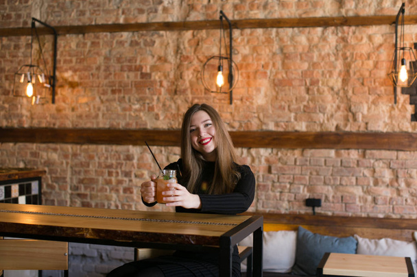 A pohár limonádé kávézó közelében fából készült asztal ül, és pihentető elégedett lány. - Fotó, kép