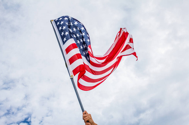 Hand hält amerikanische Flagge hautnah vor blauem Himmel mit Wolken - Foto, Bild