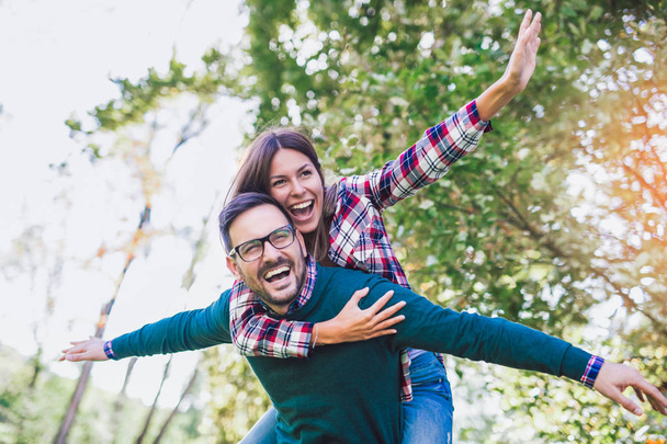 Pareja divirtiéndose hombre dando piggyback a mujer en otoño parque
 - Foto, Imagen