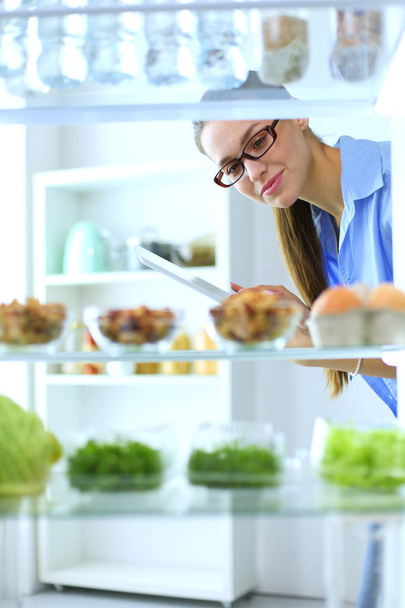Portrait of female standing near open fridge full of healthy food, vegetables and fruits. Portrait of female - Foto, afbeelding