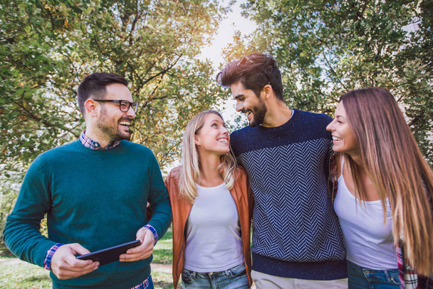 Obraz z czterech szczęśliwy uśmiechający się młodych przyjaciół spaceru na świeżym powietrzu w parku trzymając tablet cyfrowy - Zdjęcie, obraz