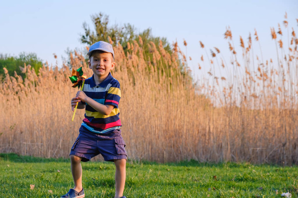 Niño jugando con molino de viento en la hierba verde de la playa en el concepto de vacaciones de verano para la libertad
 - Foto, imagen
