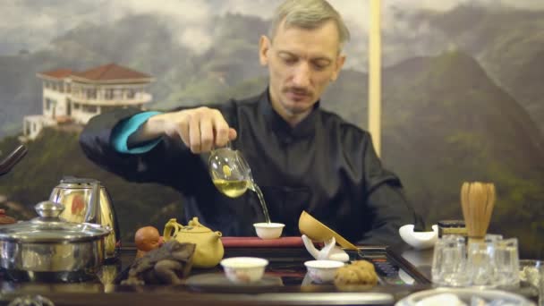 Podczas ceremonii parzenia herbaty. Mistrz mężczyzna leje zielona herbata z dzbanek do herbaty szkło do białego kubka - Materiał filmowy, wideo