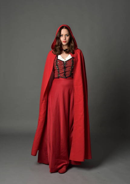 マント、灰色のスタジオの背景に立ちポーズで赤のファンタジー衣装を着てブルネットの女性の完全な長さの肖像画. - 写真・画像