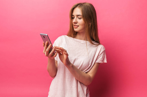 Portrait of cheerful beautiful girl watching the phone, texting, isolated on pink background, advertising - Valokuva, kuva