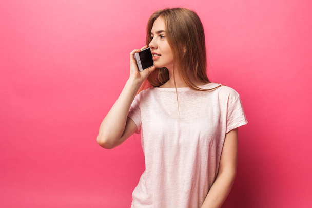 Portrait of cheerful beautiful girl talking on phone, looking away, funny enough, isolated on pink background, advertising - Photo, Image