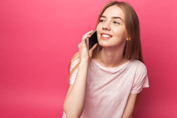 Portrait of cheerful beautiful girl talking on phone, looking away, funny enough, isolated on pink background, advertising - Zdjęcie, obraz