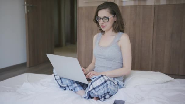 Woman in pajamas using laptop in bedroom - Кадры, видео