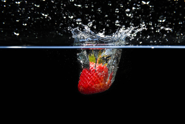 Strawberry falling into the water and splashing drops on black b - Zdjęcie, obraz
