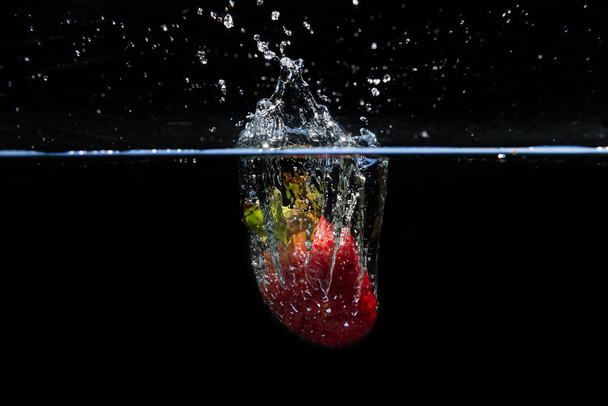 Strawberry falling into the water and splashing drops on black b - 写真・画像