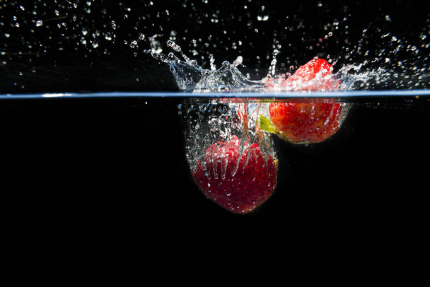 Strawberries falling into the water and splashing drops on black background - Fotó, kép