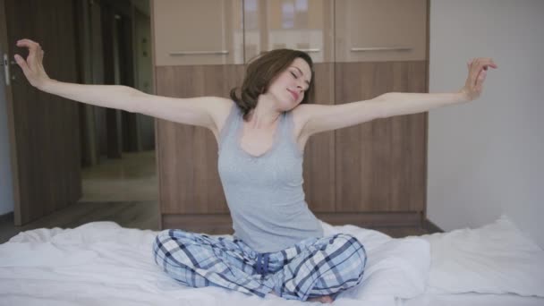 Atrakcyjna kobieta siedzi na łóżku i rozciąganie - Materiał filmowy, wideo