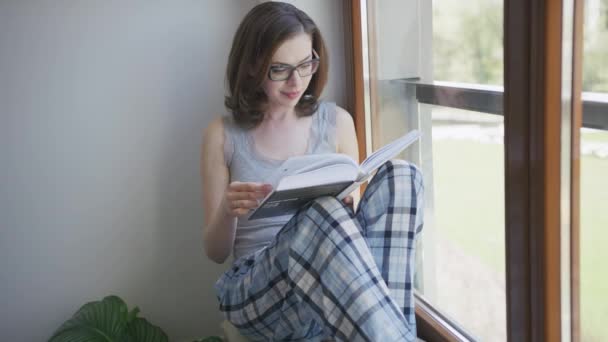 Молода жінка сидить у вікні вдома і читає
 - Кадри, відео