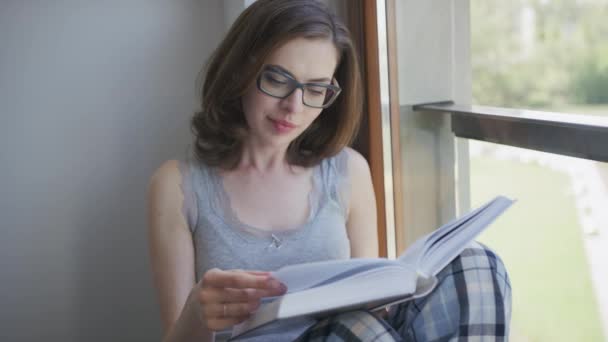 Attractive woman sitting by window and reading - Footage, Video