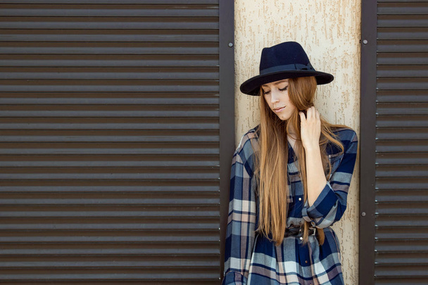 Zrzavé vlasy holka v kostkované košili a vintage klobouk, s pozicí hnědý batoh na ulici. Módní a stylový koncept. - Fotografie, Obrázek