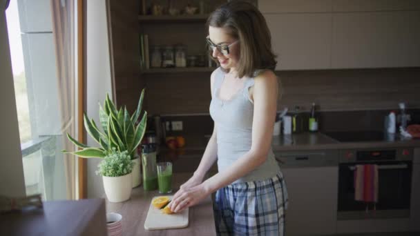 Atrakcyjna kobieta cięcia orange stoi w kuchni - Materiał filmowy, wideo