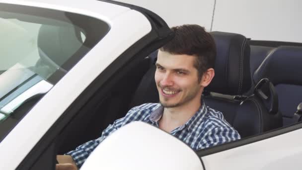 Przystojny szczęśliwy młody kierowca-mężczyzna trzyma kluczyki do samochodu siedzi w jego auto - Materiał filmowy, wideo