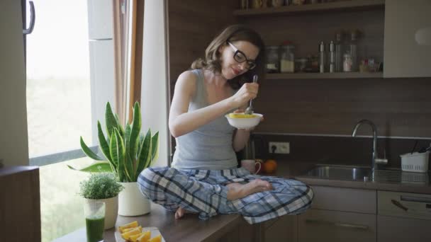 Atrakcyjna kobieta siedzi na stole i jedzenie śniadanie - Materiał filmowy, wideo