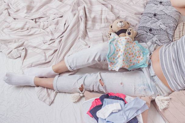 Zwangere vrouw met een teddybeer en diverse kleding voor een pasgeborene - Foto, afbeelding