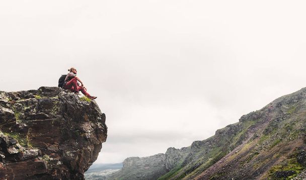 Nuori komea retkeilijä mies istuu päälle ja nauttia näkymä vuoristolaaksoon
 - Valokuva, kuva