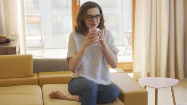 Woman with mug sitting on couch - Video, Çekim