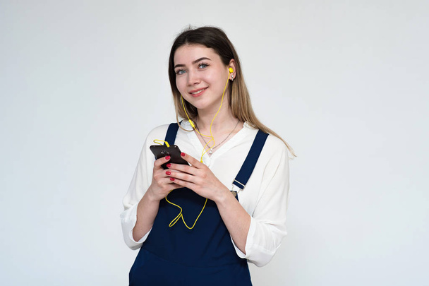 Portrait of a beautiful and young girl on a white background listening to music from a smartphone. - Fotoğraf, Görsel