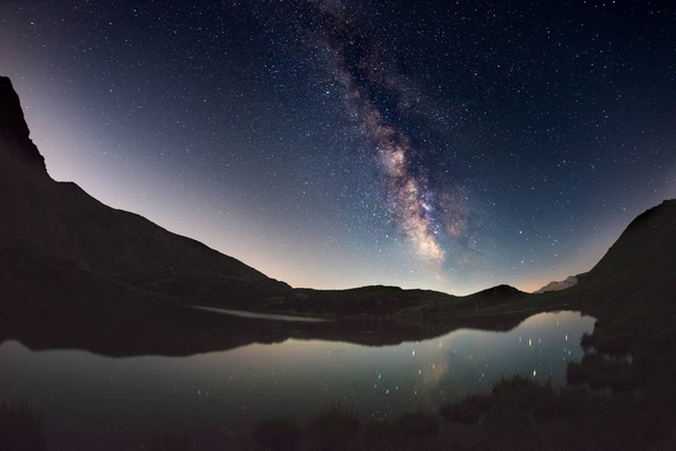 Arco de la Vía Láctea y cielo estrellado reflejado en el lago a gran altitud en los Alpes. Distorsión escénica de ojo de pez y vista de 180 grados
. - Foto, imagen