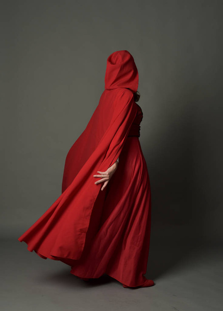 full length portrait of brunette lady wearing red fantasy costume with cloak, standing pose on grey studio background. - Photo, Image