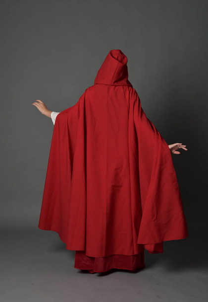 full length portrait of brunette lady wearing red fantasy costume with cloak, standing pose on grey studio background. - Foto, Imagen
