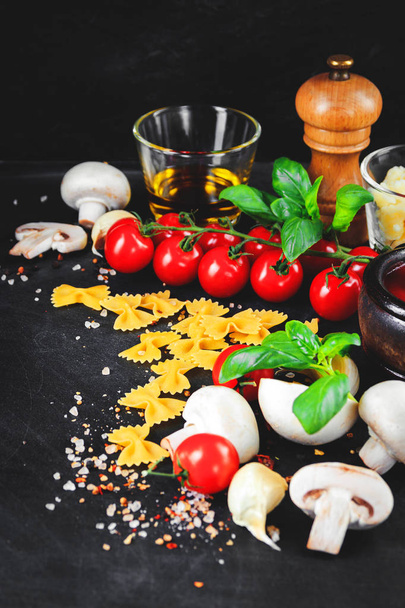 Італійська паста інгредієнтів. Вишневі помідори, farfalle макаронних виробів, часник, гриби, базилік, оливкова олія, моцарелла і спецій на тлі темно гранж - Фото, зображення