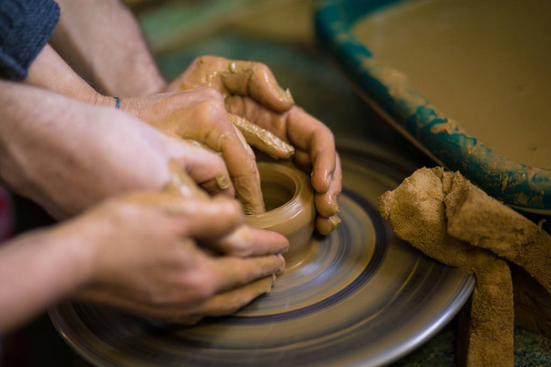 Close-up handen van potter in schort vaas van klei, selectieve aandacht maken. Daarmee samen. Bovenaanzicht van potter onderwijzen van kind tot en met keramische pot op aardewerk wiel maken - Foto, afbeelding