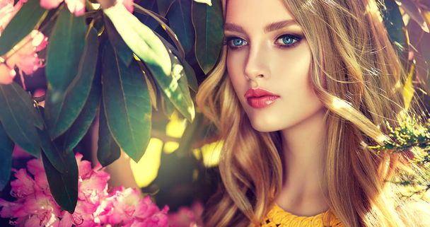 Piękna wiosna dziewczyna w pachnące kwiaty różowe w parku kwitnąć lato. Kobieta w kwitnący ogród. Moda, kosmetyki & perfumy. Kręcone blond włosy - Zdjęcie, obraz