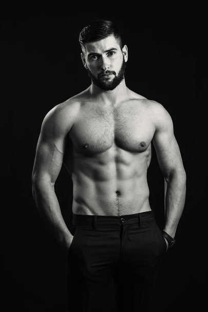 Young handsome muscular man with a beard, posing on a black back - Foto, Bild