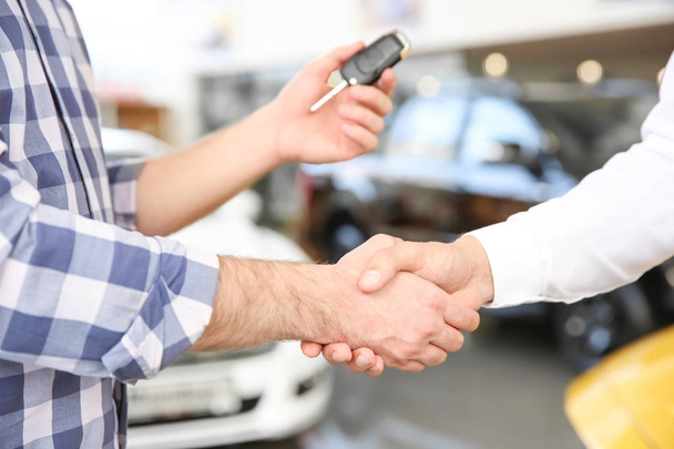 Young man shaking hands with salesman in car salon - Foto, Bild