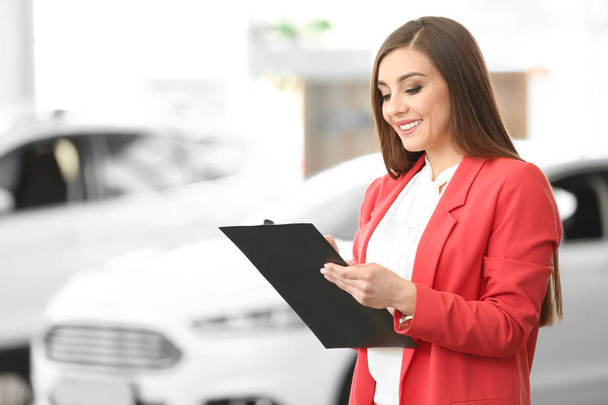 Young woman with clipboard in car salon - Foto, Imagem