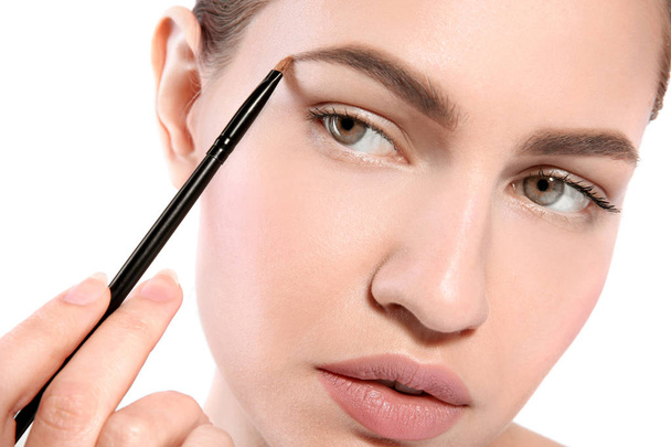Beautiful woman with perfect eyebrows applying makeup on light background - Фото, зображення