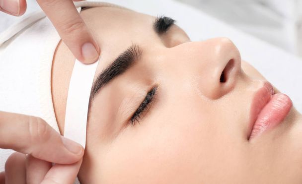 Young woman having professional eyebrow correction procedure in beauty salon, closeup - Фото, изображение