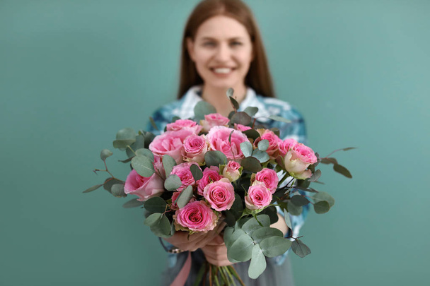Female florist holding bouquet of beautiful flowers on color background - Фото, зображення