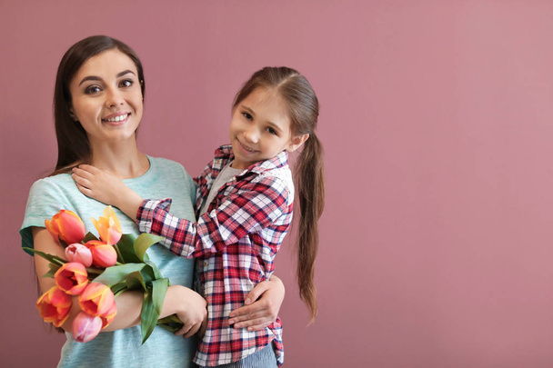 Portrait of happy woman with flowers and her daughter on color background. Mother's day celebration - Foto, afbeelding