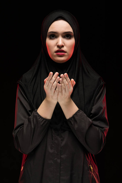 Muotokuva kaunis vakava nuori musliminainen yllään musta hijab kädet lähellä hänen kasvonsa rukoilee käsite mustalla pohjalla
 - Valokuva, kuva