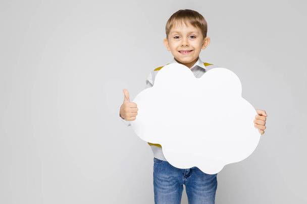 雲の形の白いポスターを保持している灰色の背景の上に立って小さな男の子の肖像画 - 写真・画像