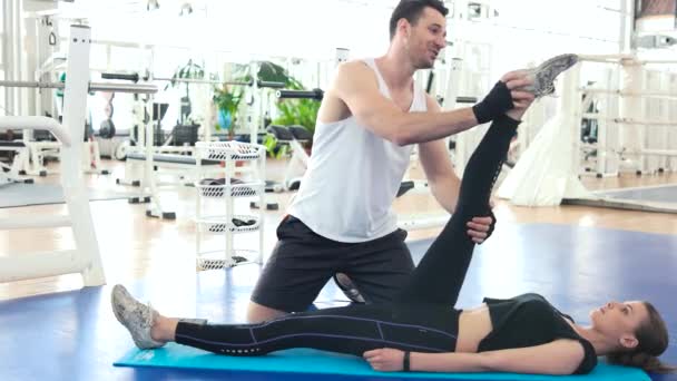 Γυμναστήριο εκπαιδευτής τεντώνει πόδι της νεαρής γυναίκας. - Πλάνα, βίντεο
