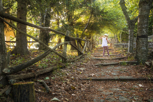 Een klein meisje in een hoed loopt langs het bospad. Zonsondergang in een forest fairy. - Foto, afbeelding