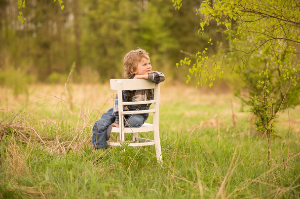 Fiatal szőke fiú pihentető fehér öreg szék alatt álló nyírfa szabadban. - Fotó, kép
