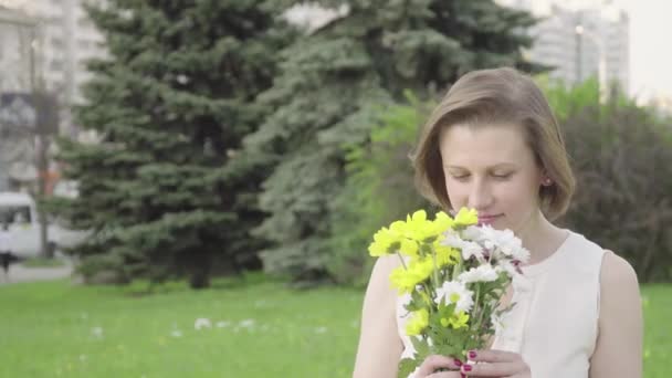 Portrait of a pretty young woman sniffing a bouquet. Beautiful woman inhales the fragrance of flowers - Felvétel, videó