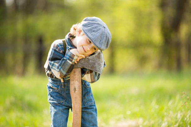 Маленький білий хлопчик в капелюсі позує з великою сокирою. Портрет дрібного лісоруба
 - Фото, зображення