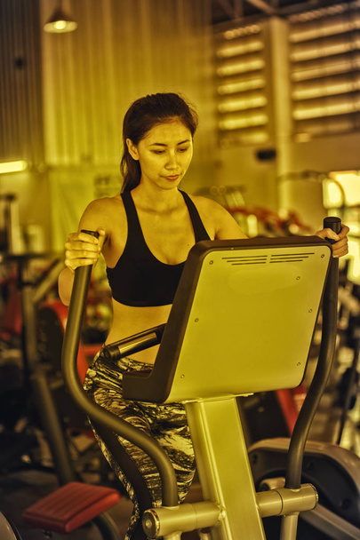 ázsiai fiatal nő csinál gyakorlat -on egy elliptikus edző -ban fitnesz terem - Fotó, kép