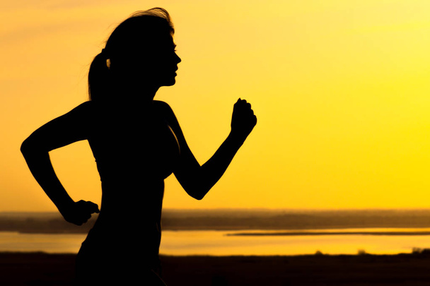 Silhouette einer Frau, die bei Sonnenuntergang in der Natur joggt, weibliches Sportprofil, Konzept für Sport, Freizeit und Gesundheit - Foto, Bild