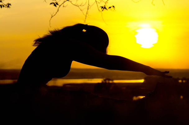 Silhouette einer jungen Frau, die sich bei Sonnenuntergang in der Natur fit hält, ein sportliches weibliches Profil, das Konzept von Sport und Gesundheitspflege - Foto, Bild