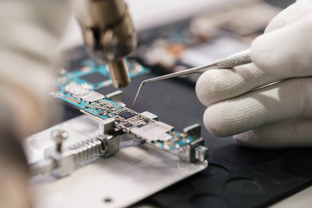 Work with a soldering iron. Microelectronics device. Close-up hands of a service worker repairing modern smartphone. Repair and service concept. - Foto, afbeelding